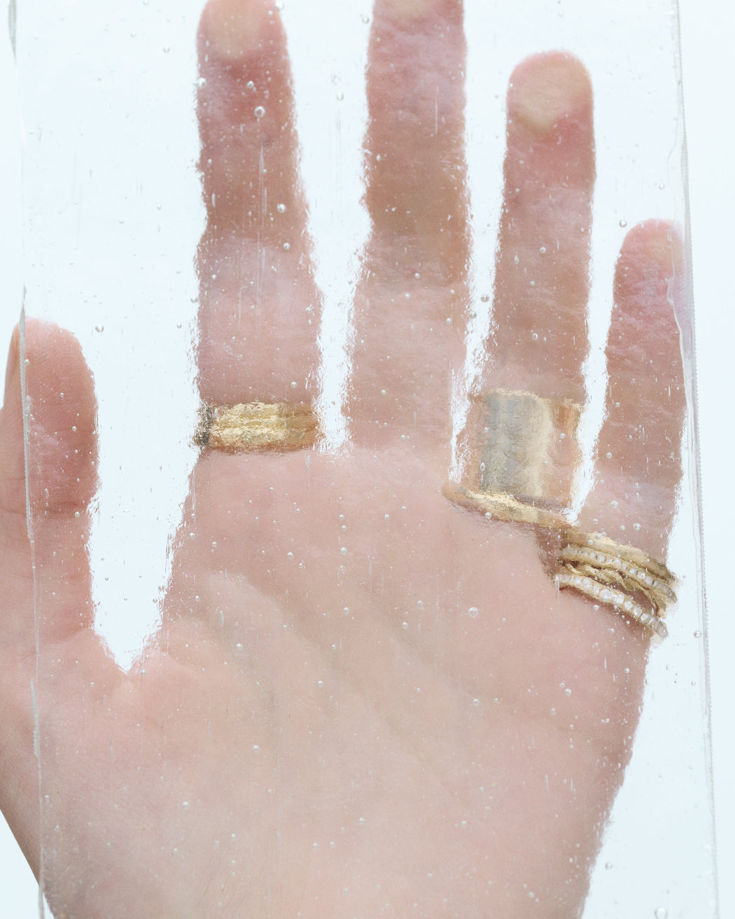 Hand wearing multiple gold Shihara rings on a clear background